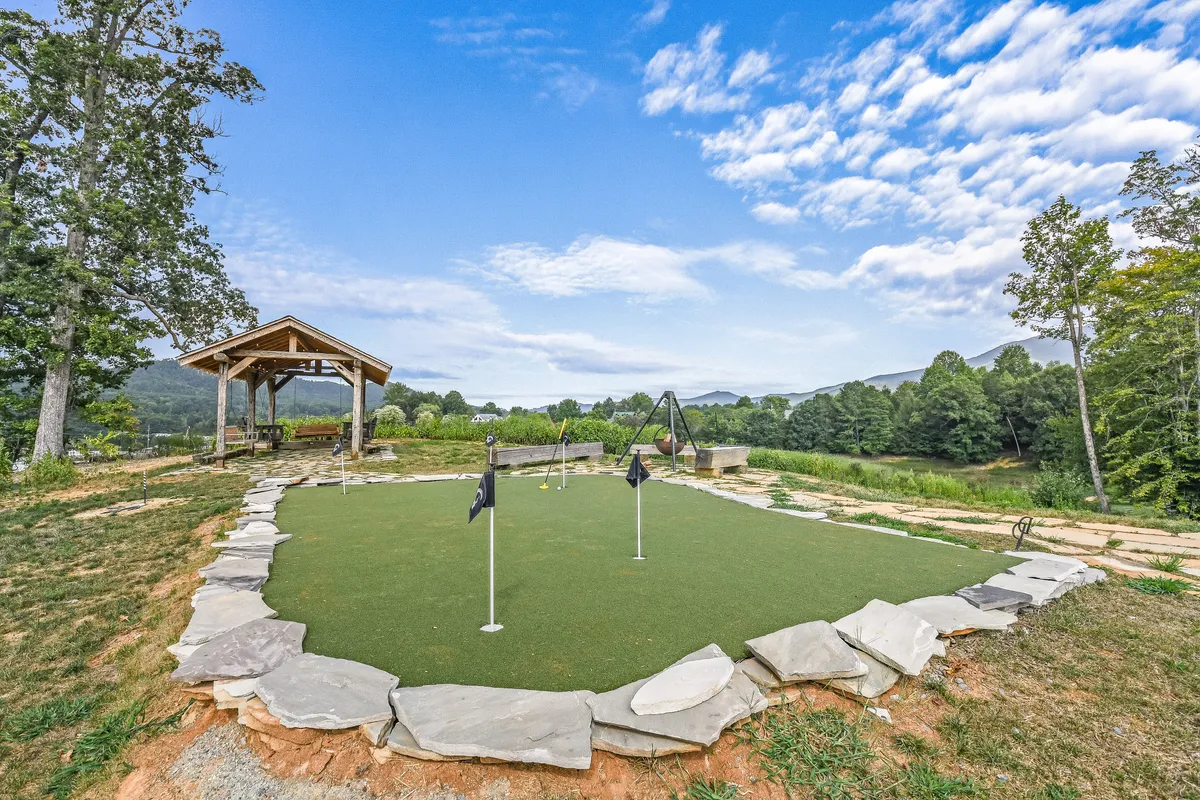 A vibrant outdoor scene with a 5-hole putting green, a wooden gazebo nestled among lush greenery, and a sweeping mountain backdrop. Family members enjoy golf practice and leisure time in and around the gazebo, creating an atmosphere of playful relaxation.