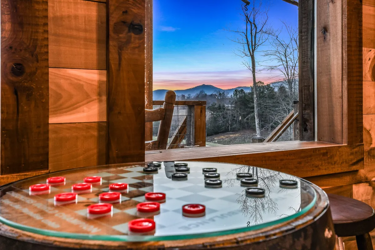 A cozy lofted table area with a checkerboard set up for board games, warm wooden interiors, and a sunset view through the window. The scene captures players enjoying board games in a relaxed setting.