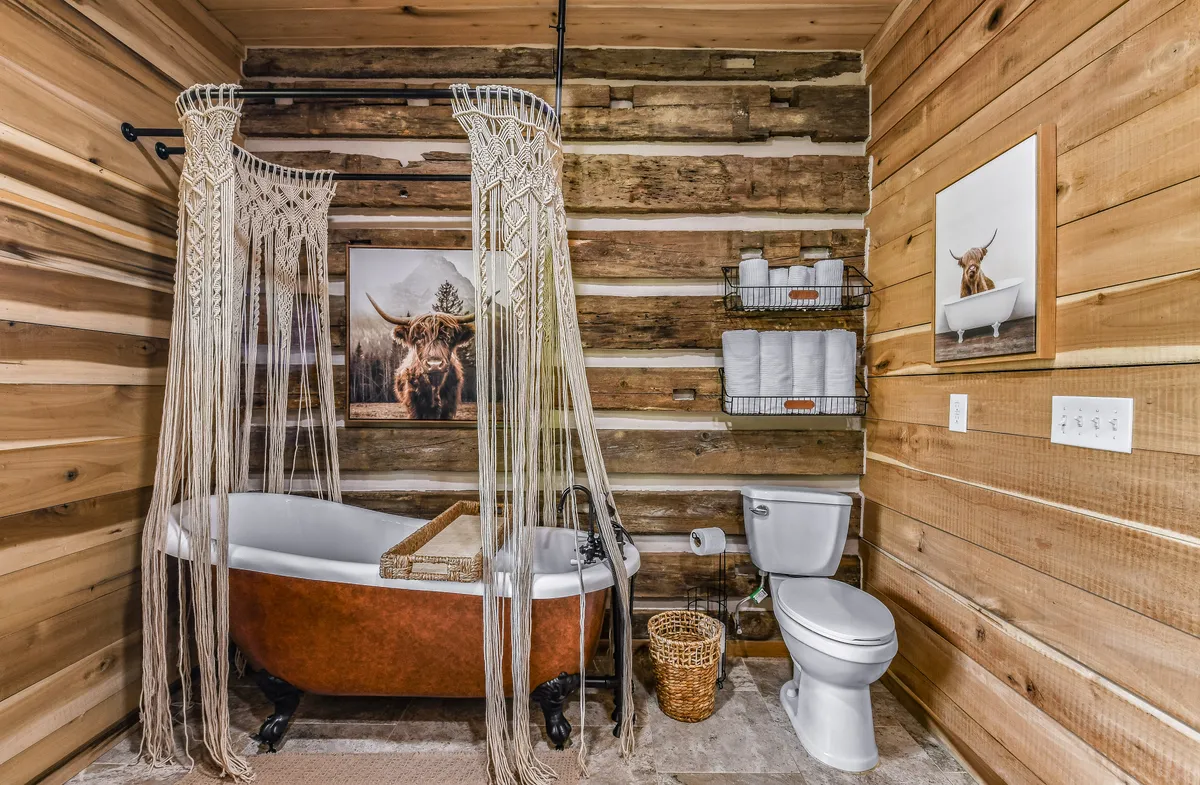 A calming bathroom scene with a freestanding bathtub, macrame curtain, wooden wall, and decorative cow artwork. The setting invites leisurely baths and self-care, embodying the spa-like retreat highlighted in the section.