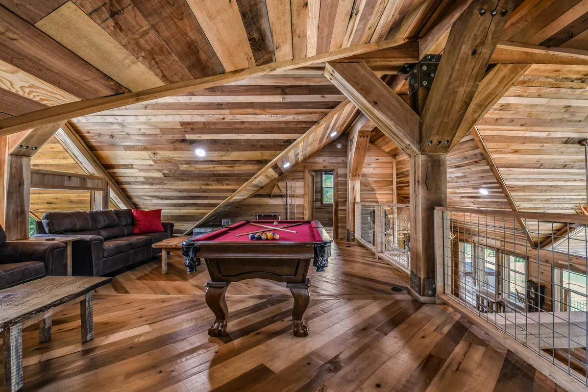 An inviting interior game room featuring a pool table, comfy sofa, and rustic wooden beams. The space feels lively and is clearly set up for friendly competition and fun family nights indoors.