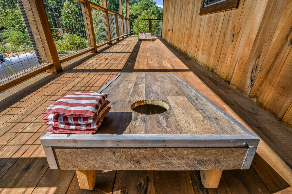 A playful scene focused on a cornhole game board set up outdoors, with a stack of towels suggesting pool or lawn games nearby. The setting is bright and sunny, ideal for friendly tournaments and outdoor fun.