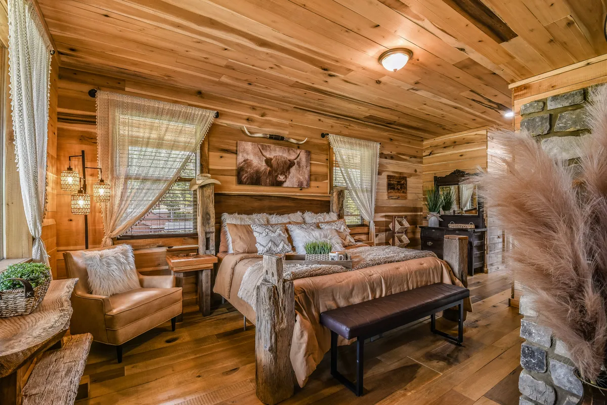 A tranquil bedroom with a wooden bed frame, textured bedding, potted plants, artwork on the wall, and gentle natural light streaming through the windows. The setting feels peaceful and rejuvenating, perfect for recharging in privacy.